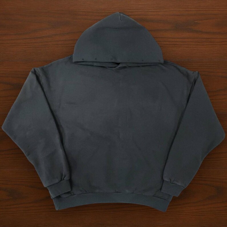 May include: A dark gray hoodie with a hood, long sleeves, and a ribbed hem and cuffs. The hoodie is made of a soft, comfortable material and is suitable for casual wear. The garment is displayed on a wooden surface.
