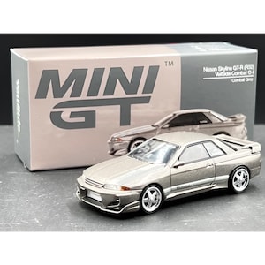 Könnte beinhalten: Ein Modellauto eines Nissan Skyline GT-R (R32) VeilSide Combat in Gimbal Grey. Das Modellauto steht vor seiner Box mit dem Logo "MINI GT" und den Details des Autos.