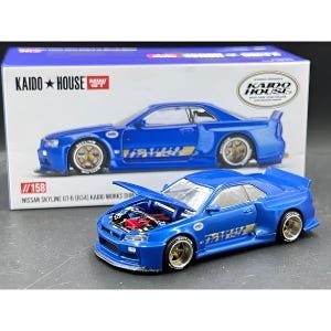 May include: A blue Nissan Skyline GT-R (R34) Kaido Works Shin diecast model car with the hood open, revealing the engine. The model is displayed in front of its packaging, which also features the car. The text "KAIDO HOUSE" and "1/158" are visible.