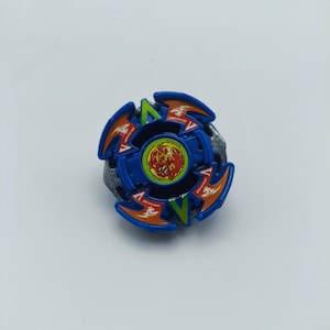 May include: A blue, orange, and green spinning top toy with a central design featuring a red and yellow image. The toy has a circular design with multiple blades and a metallic grey base. The toy is designed for spinning.