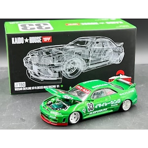 Op de afbeelding: Een groene Nissan Skyline GT-R (R33) IMAI Racing V1 modelauto met de motorkap open, waardoor de motor zichtbaar is. Het model heeft nummer 33 en Japanse tekst. De doos toont een diagram van de auto en de tekst "KAIDO HOUSE MINI GT".