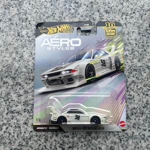 May include: A Hot Wheels Premium Aero Styles Nissan R32 Skyline GT-R die-cast toy car in white with black racing wheels and the number 58 on the side. The car is packaged in a blister card featuring an illustration of the vehicle and text.