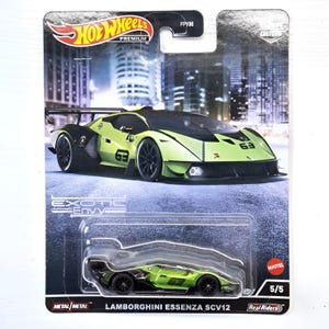 Op de afbeelding: Een Hot Wheels Premium modelauto van een Lamborghini Essenza SCV12. De auto is voornamelijk limoengroen en zwart, met het nummer "63". De verpakking toont het logo van de "Exotic Envy"-serie en "Real Riders"-banden.