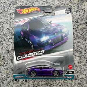 Puede incluir: Un paquete de coche de juguete Hot Wheels con un Volkswagen Corrado morado. El embalaje incluye los logotipos Hot Wheels Premium y Car Culture, con las palabras "Modern Classics". El coche es un modelo 4/5 con neumáticos Real Riders.