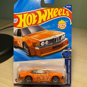 Puede incluir: Coche de juguete Hot Wheels naranja con ruedas negras. El coche tiene el número 35 y el texto "Castrol" en el lateral. El embalaje incluye el logotipo de Hot Wheels, el año 2025 y el texto "WILD WIDEBODY CARROSSERIES LARGES ET FÉROCES".