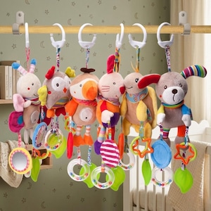 May include: A collection of colorful plush baby toys, each featuring a different animal design, including a bunny, owl, and dog. The toys hang from a wooden bar and include attached rings, mirrors, and other sensory elements.