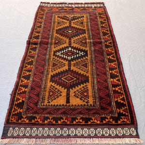 May include: Rectangular rug with a central geometric design in shades of brown, orange, and black. The rug features a border with repeating patterns and a fringed edge. The rug's design is symmetrical and traditional.