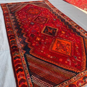 May include: A rectangular area rug featuring a vibrant red background with intricate geometric patterns in black, orange, and deep brown. The design includes multiple central diamond-shaped medallions and a detailed border with repeating motifs.