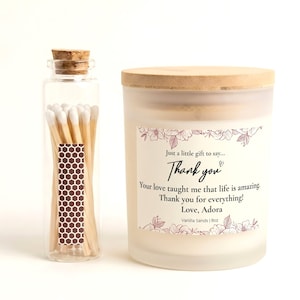 May include: A clear glass match bottle with a cork stopper and a brown honeycomb design. Next to it is a frosted glass candle with a wooden lid. The candle has a label that says "Thank you" and "Vanilla Sands | 8oz."