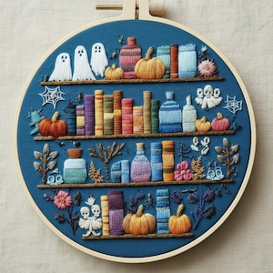 Peut inclure: Un tambour à broder circulaire sur fond de tissu bleu foncé avec quatre étagères horizontales brodées en fil marron. Les étagères présentent des livres, des citrouilles, des fantômes, des crânes, des toiles d'araignée et des fleurs.