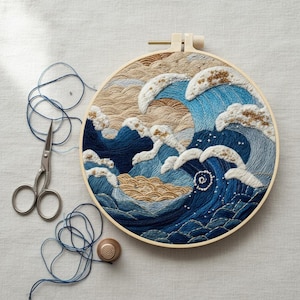 May include: A round embroidery hoop featuring a detailed wave design in shades of blue, beige, and white. The artwork is accompanied by blue thread, a pair of scissors, and a wooden thimble. The embroidery captures the essence of a seascape.