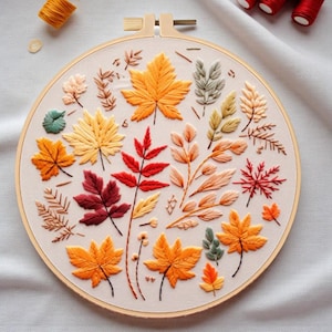 Peut inclure: Un cercle à broder avec des feuilles d'automne colorées. Les feuilles sont brodées en jaune, orange, rouge et vert sur un tissu crème. Le cercle à broder en bois est un artisanat sur le thème de l'automne.