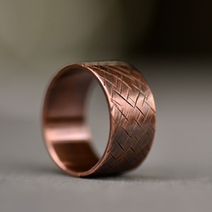 May include: A copper ring with a textured, woven pattern. The ring is wide and has a polished finish.