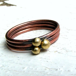 May include: A copper ring with three gold beads. The ring is made of three bands of copper wire.