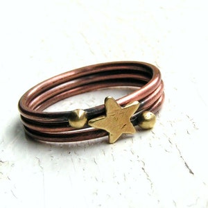 May include: A copper ring with three bands and a gold star charm. The ring has two gold beads on either side of the star.