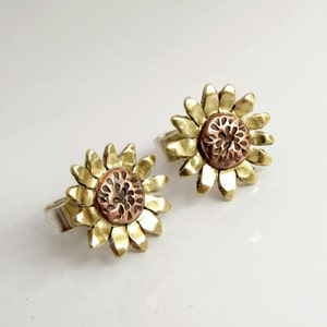May include: A pair of gold sunflower earrings with a copper centre. The earrings are made of metal and have a textured finish.