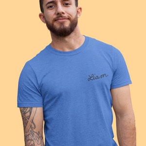 May include: A blue crew neck t-shirt with the name "Liam" in a cursive font on the chest. The shirt is a solid color and appears to be made of a soft material.