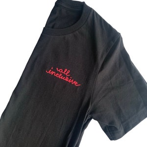 May include: Black crew neck t-shirt with the embroidered text "all inclusive" in red script on the left chest. The shirt is made of a soft, dark fabric and has short sleeves.