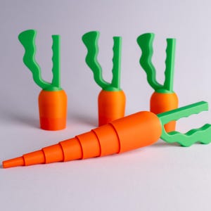 May include: Orange and green carrot-shaped kitchen tools. One is fully assembled, while others are disassembled. The tools have a bright orange carrot body and green handles. The tools are designed to resemble carrots.