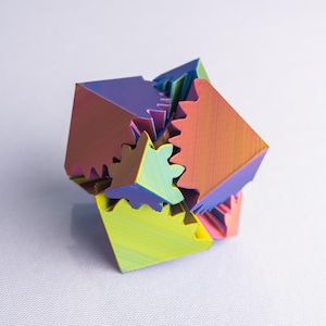 May include: A multi-colored, geometric puzzle with interlocking pieces. The puzzle features a vibrant spectrum of colors, including purple, orange, yellow, and green. The cube-shaped pieces have a gear-like design, creating an intricate and visually appealing structure.