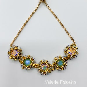 May include: A gold beaded bracelet with a sliding clasp and five square-shaped charms. Each charm features a clear iridescent stone surrounded by gold beads.