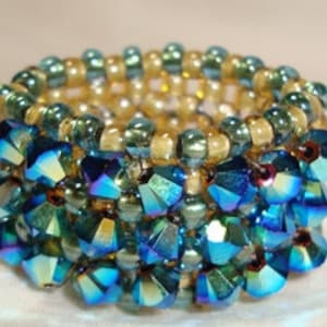 May include: A beaded ring with a multi-layered design. The bottom layer is made of blue iridescent beads, the middle layer is made of gold beads, and the top layer is made of green beads.