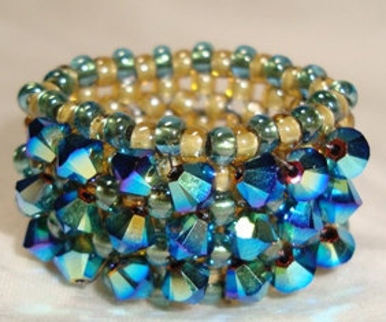 May include: A beaded ring with a multi-layered design. The bottom layer is made of blue iridescent beads, the middle layer is made of gold beads, and the top layer is made of green beads.