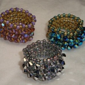 May include: Three beaded rings with a gold base and different colored crystal tops. The rings are purple, blue, and silver.