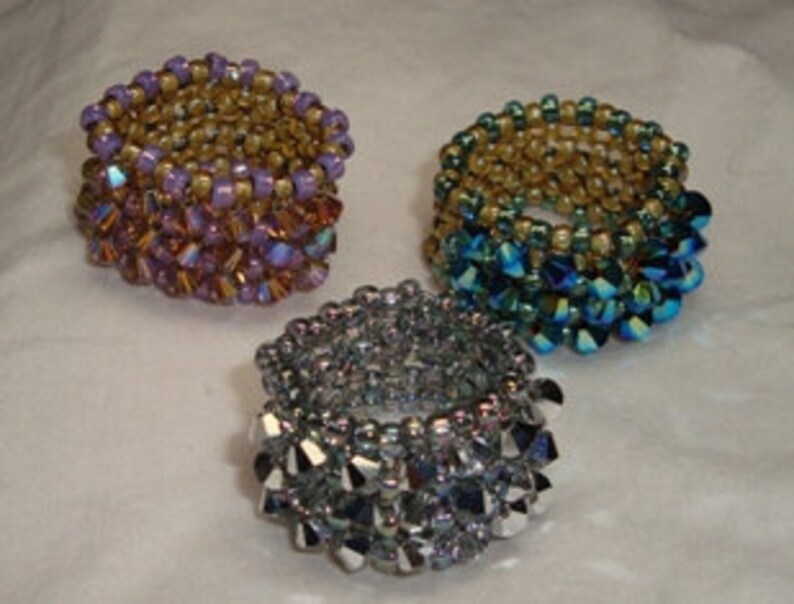 May include: Three beaded rings with a gold base and different colored crystal tops. The rings are purple, blue, and silver.