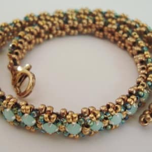 Pode incluir: Um bracelete de contas douradas e verdes com fecho de encaixe. O bracelete é feito com contas pequenas e redondas e apresenta contas maiores de cor verde claro.