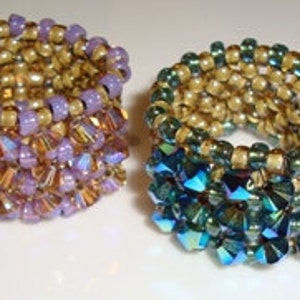 May include: Two beaded rings, one with purple and gold beads and the other with green and gold beads.