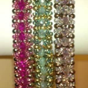Puede incluir: Tres pulseras de cuentas, una rosa, una verde y una plateada, apiladas una encima de la otra.