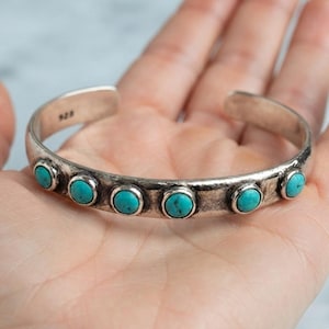 Può includere: Un bracciale a fascia in argento con sei pietre turchesi rotonde tagliate a cabochon disposte in fila lungo il cinturino. Il metallo ha una finitura invecchiata e ossidata e l'interno del bracciale reca il marchio 925 per l'argento sterling.