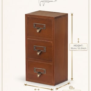 May include: A brown wooden apothecary organizer with three drawers, each featuring a brass-toned metal label holder and pull handle. The unit measures 12.2 inches in height, 6.89 inches in width, and 5.51 inches in depth, as shown in the dimension guide.