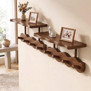 May include: A two-tiered wall-mounted wooden shelf unit featuring a wavy, scalloped design along the base with multiple cylindrical pegs for hanging items. The shelves are dark brown wood, holding a small vase, a white cat figurine, and two frames.