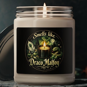 Peut inclure: Une bougie blanche dans un bocal en verre avec une étiquette noire. L'étiquette indique "Smells like Draco Malfoy" avec un graphique d'une bougie allumée, de plumes et d'autres éléments. Le couvercle est sur le côté.