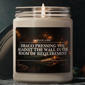May include: A lit, white candle in a clear glass jar with a silver lid. The label reads "Smells Like Draco Pressing You Against The Wall In The Room Of Requirement."