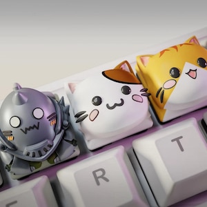 May include: Close-up of a keyboard with custom keycaps. The keycaps feature cartoon cat faces in white, orange, and brown, and a silver robot. The keyboard keys are white. The keycaps are designed to be decorative.