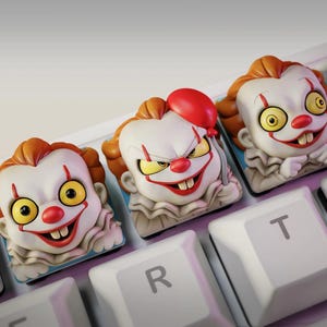 Könnte beinhalten: Drei individuelle Tastenkappen mit einem Clown-Design. Die Kappen haben weiße Gesichter, rote Nasen und Münder sowie orangefarbenes Haar. Eine Kappe hat einen roten Ballon. Die Kappen befinden sich auf einer weißen Tastatur.