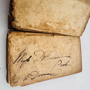 May include: An antique book with aged, yellowed pages. The cover is open, revealing handwritten script in black ink. The text reads "Mifs Durnal Book" and "Mifs A. Durnal". The book's edges show wear and tear, indicating its age.