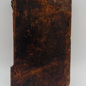 May include: A weathered, rectangular book with a distressed, brown leather cover. The cover shows signs of age with a worn texture and visible imperfections. The edges of the book are slightly frayed, adding to its antique appearance.