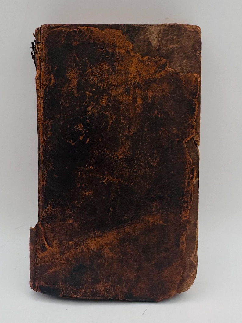 May include: A weathered, rectangular book with a distressed, brown leather cover. The cover shows signs of age with a worn texture and visible imperfections. The edges of the book are slightly frayed, adding to its antique appearance.