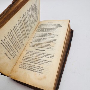 May include: An open antique book with aged, yellowed pages. The book's cover and edges show signs of wear, with a visible spine. The text is in English, with the title "Elegies" visible on one page. The book is set against a white background.