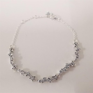 May include: A silver-toned chain bracelet featuring a series of small, star-shaped charms and circular accents embedded with clear, sparkling stones. The bracelet includes a delicate link chain and a secure lobster claw clasp closure.