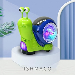 May include: A green and blue toy snail with large, googly eyes and a light-up shell. The snail has a black shell and a blue body with a light-up section. The toy is on a white pedestal. The text "ISHMACO" is at the bottom.