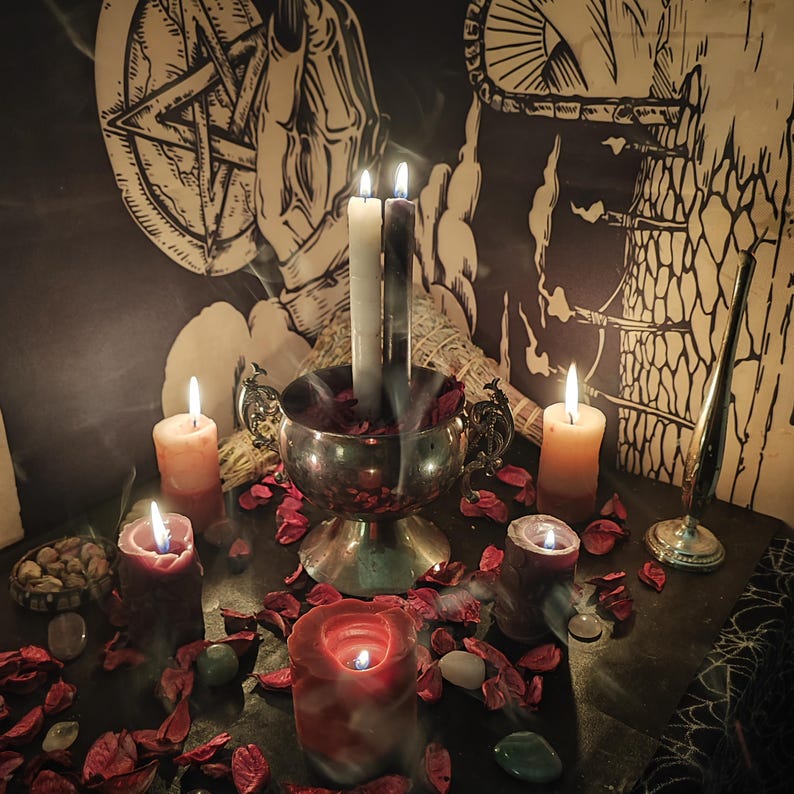 May include: A mystical scene featuring lit candles of various sizes and colors, including white, orange, and red. A silver bowl holds burning candles and red petals. The background includes a pentagram and other occult symbols, creating an atmospheric setting.