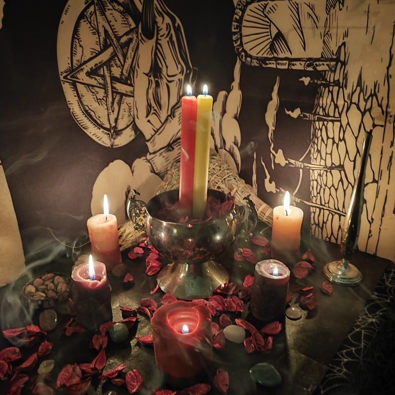 May include: A mystical scene featuring lit candles of various colors, including red, yellow, and orange. A silver bowl holds three candles, surrounded by dried rose petals and small stones. A pentagram and hand illustration are visible in the background.