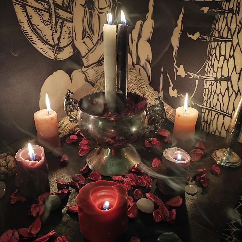 May include: A mystical scene featuring lit candles of various sizes and colors, including white, black, and red. A silver bowl holds rose petals and more candles. The background includes a tapestry with occult symbols, creating an atmospheric and spiritual setting.