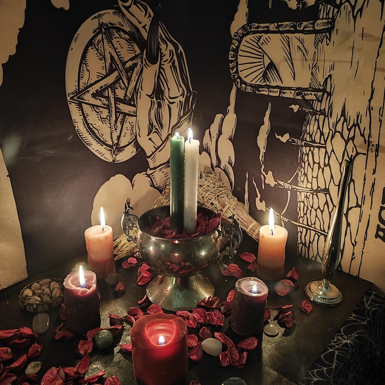May include: A mystical scene featuring lit candles of various colors, including red, orange, and green, arranged with dried rose petals and stones. A silver chalice holds candles, and a pentagram and hand illustration are visible in the background. The scene evokes a spiritual or ritualistic theme.