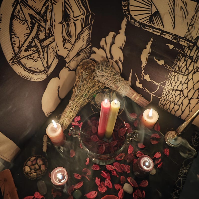 Op de afbeelding: Een mystieke sc&egrave;ne met brandende kaarsen, gedroogde kruiden en een kom met rode bloemblaadjes. Twee lange kaarsen, &eacute;&eacute;n rood en &eacute;&eacute;n geel, staan in een zilveren kom. De achtergrond is een wandtapijt met occulte symbolen.
